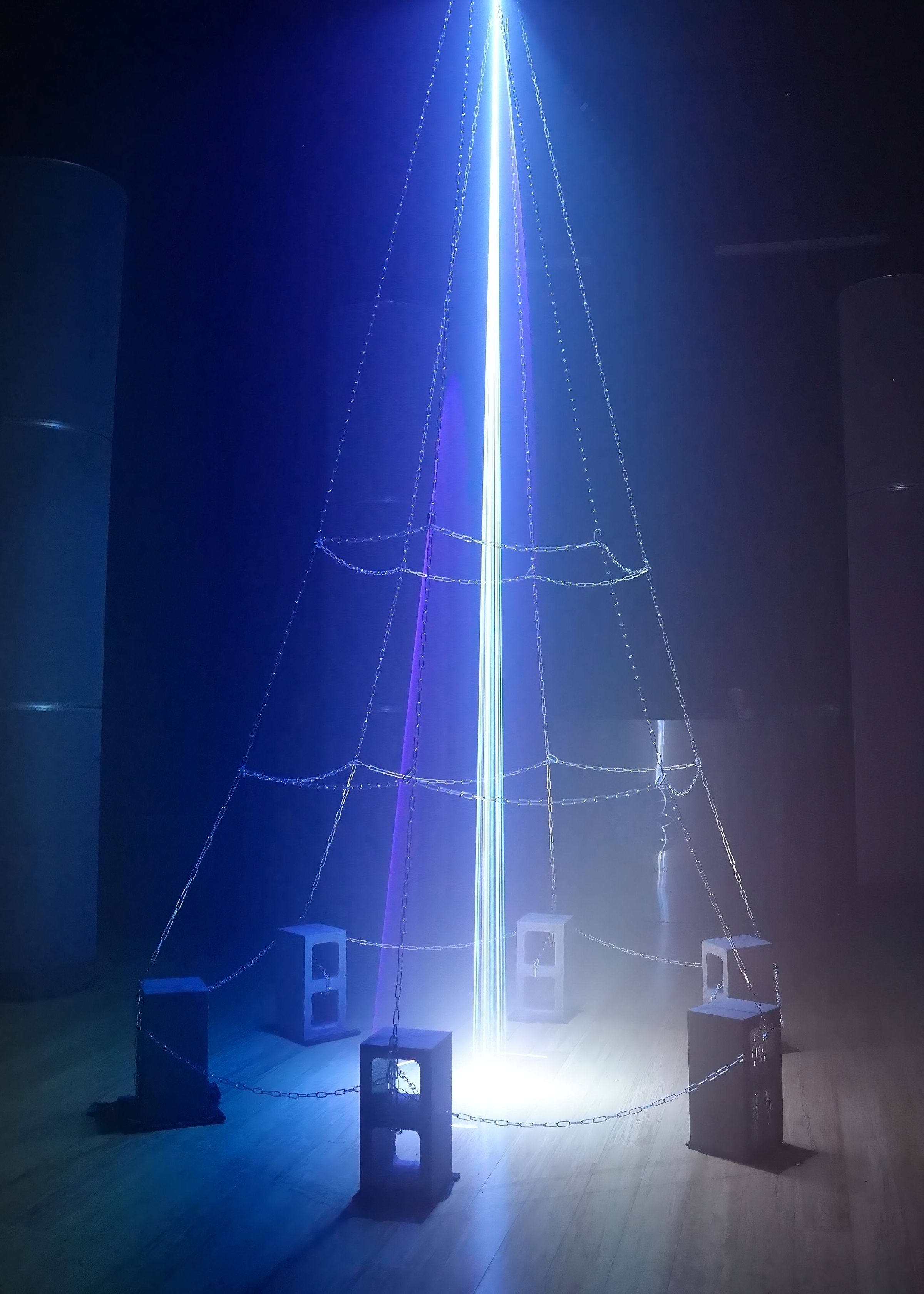 AiBeacon1: a 10-watt laser column rising from a cinderblock base ringed with chainlink, with a 32-speaker array on the floor