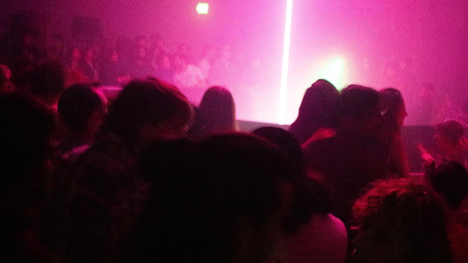 AiBeacon2: a crowd in pink haze facing a vertical laser beam over an LED array and stage light