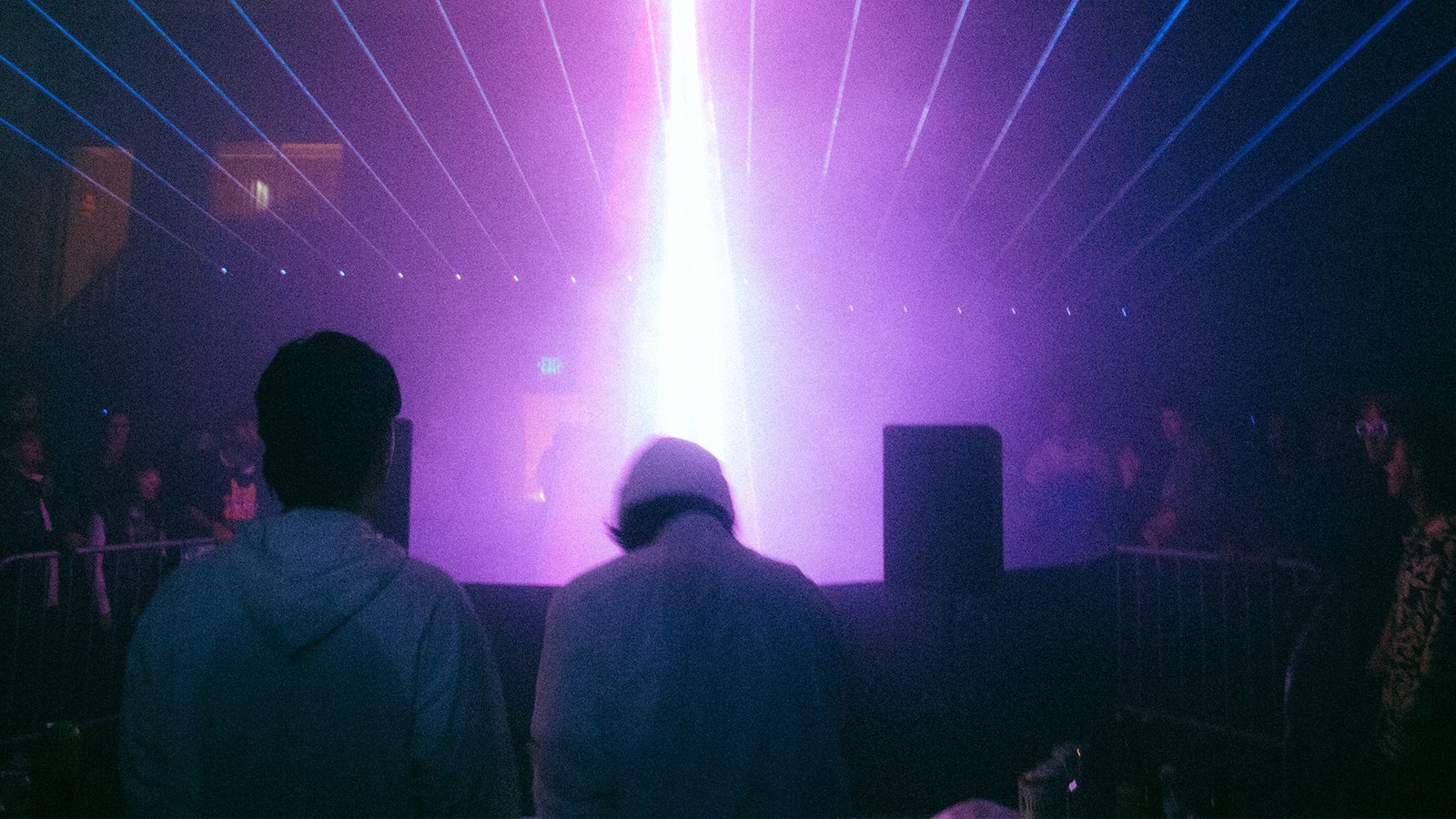 AiBeacon3: the crowd beneath a purple laser fanning across the ceiling, LED array and stage light behind an ABS plastic barricade