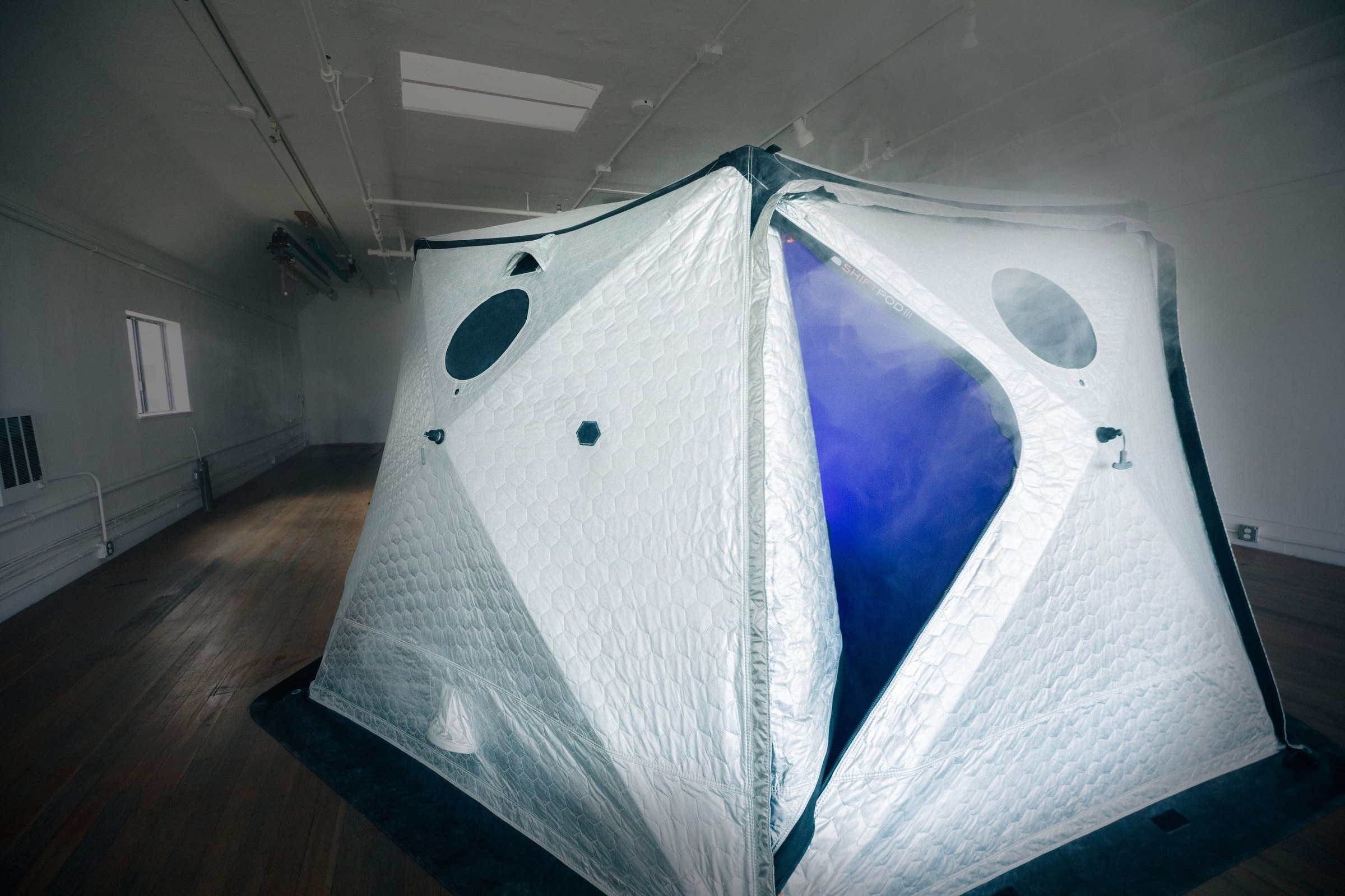 HoloDome1 seen from across the empty gallery loft, its tent glowing blue with fog pouring from the door