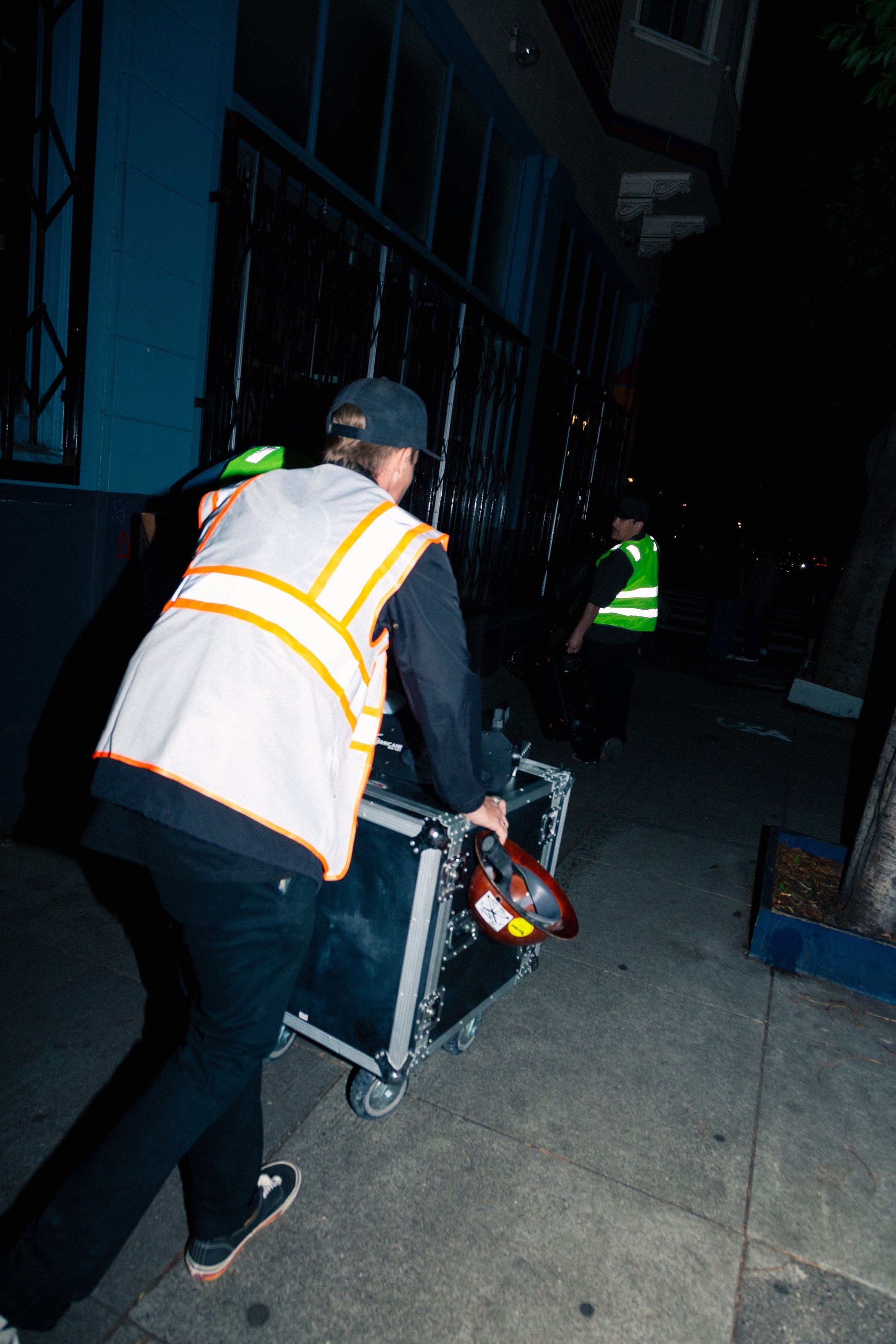 A crew member in a safety vest wheeling a generator and equipment down the sidewalk at night