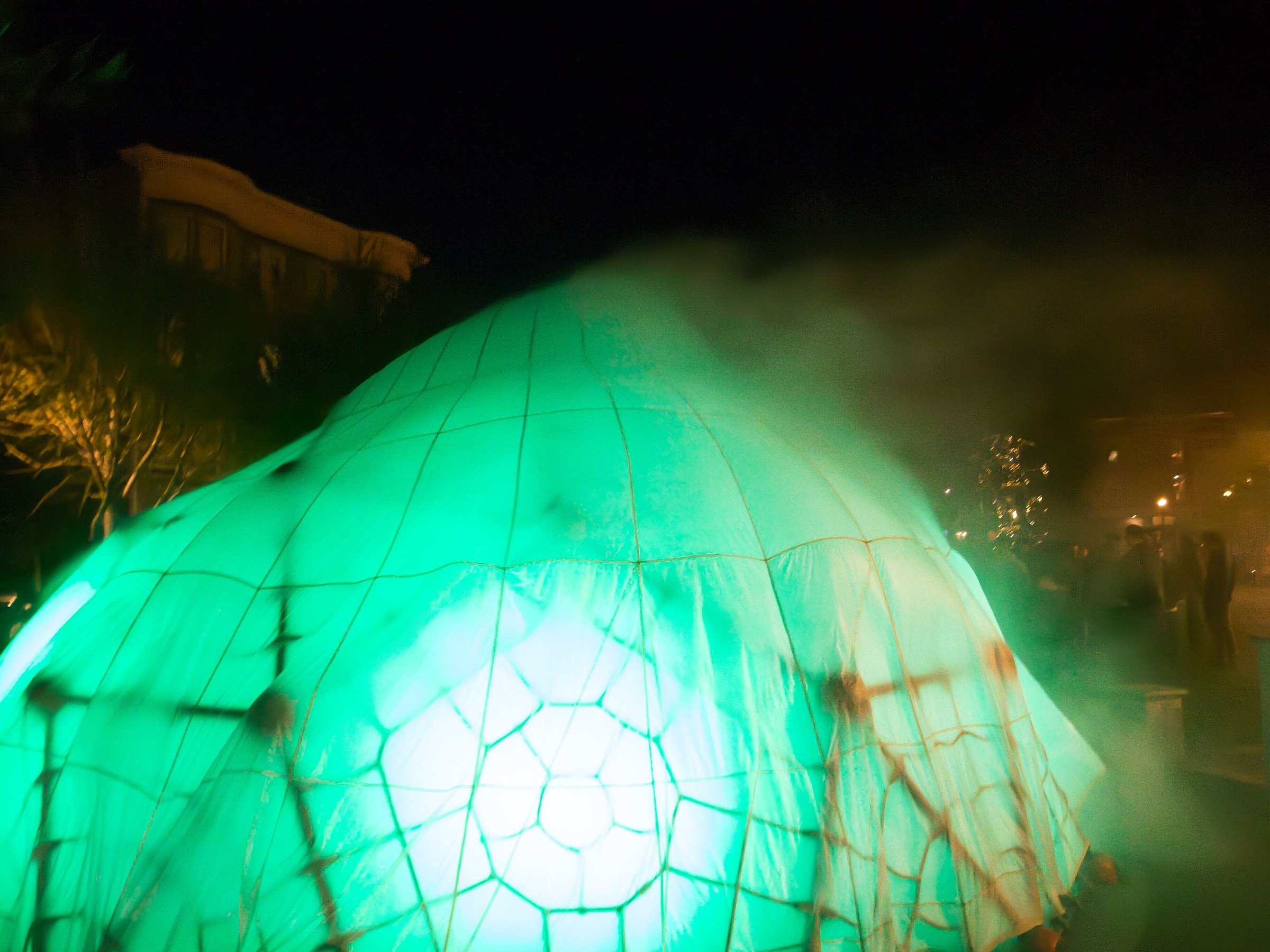 Close view of HoloDome2’s parachute skin lit green from inside, houses behind