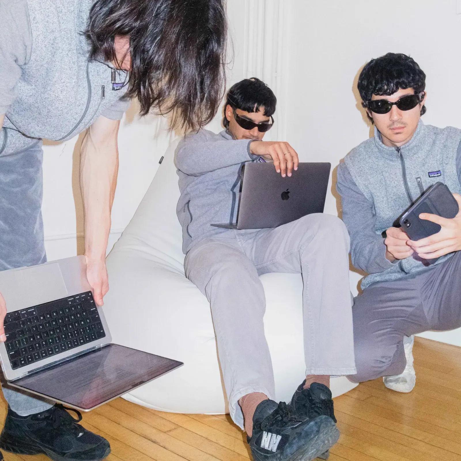 Inside the NN office: three people in grey fleece and sunglasses on a white beanbag with laptops and a tablet