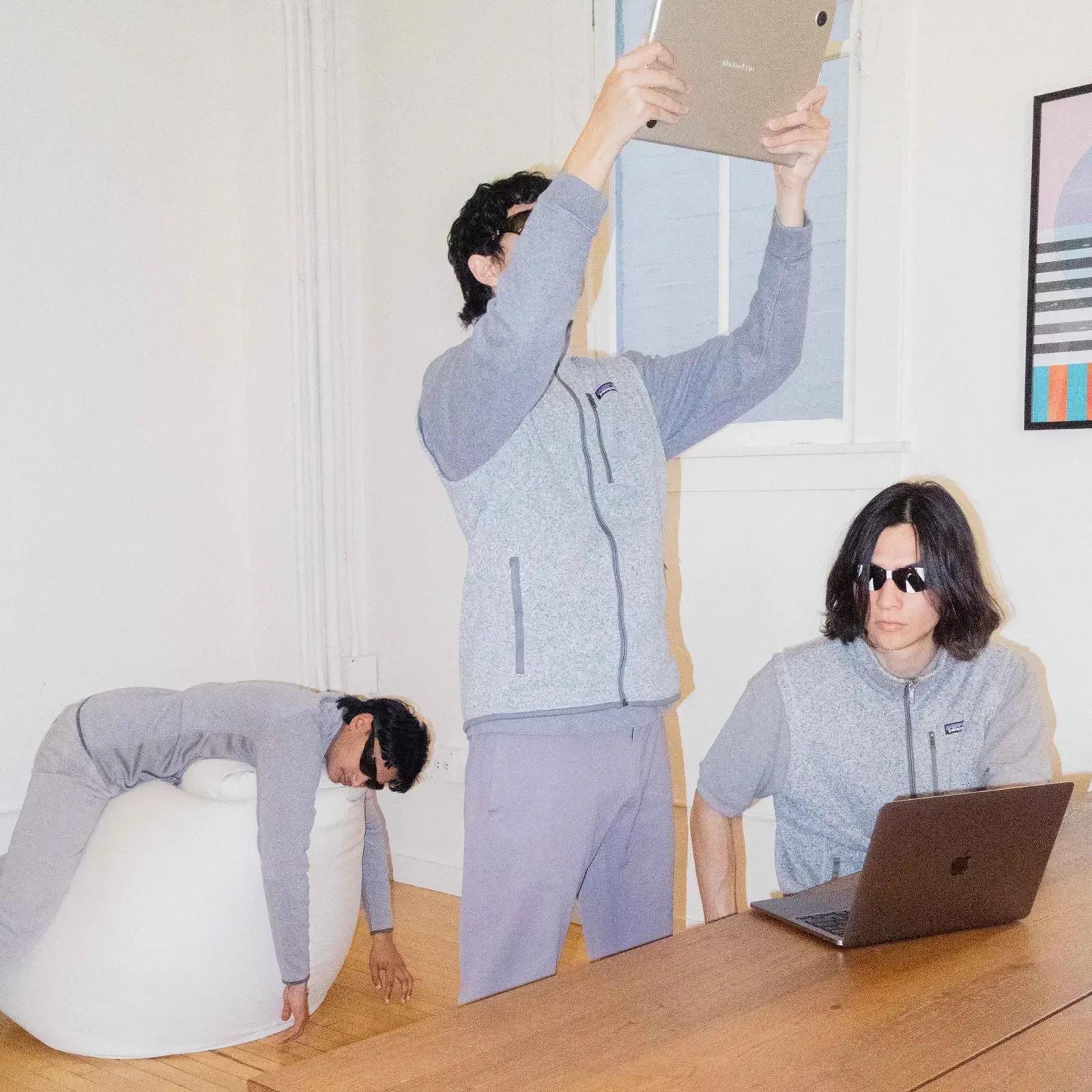 Inside the NN office: three people in grey fleece and sunglasses, one holding an iPad overhead, one at a laptop, one draped over a beanbag