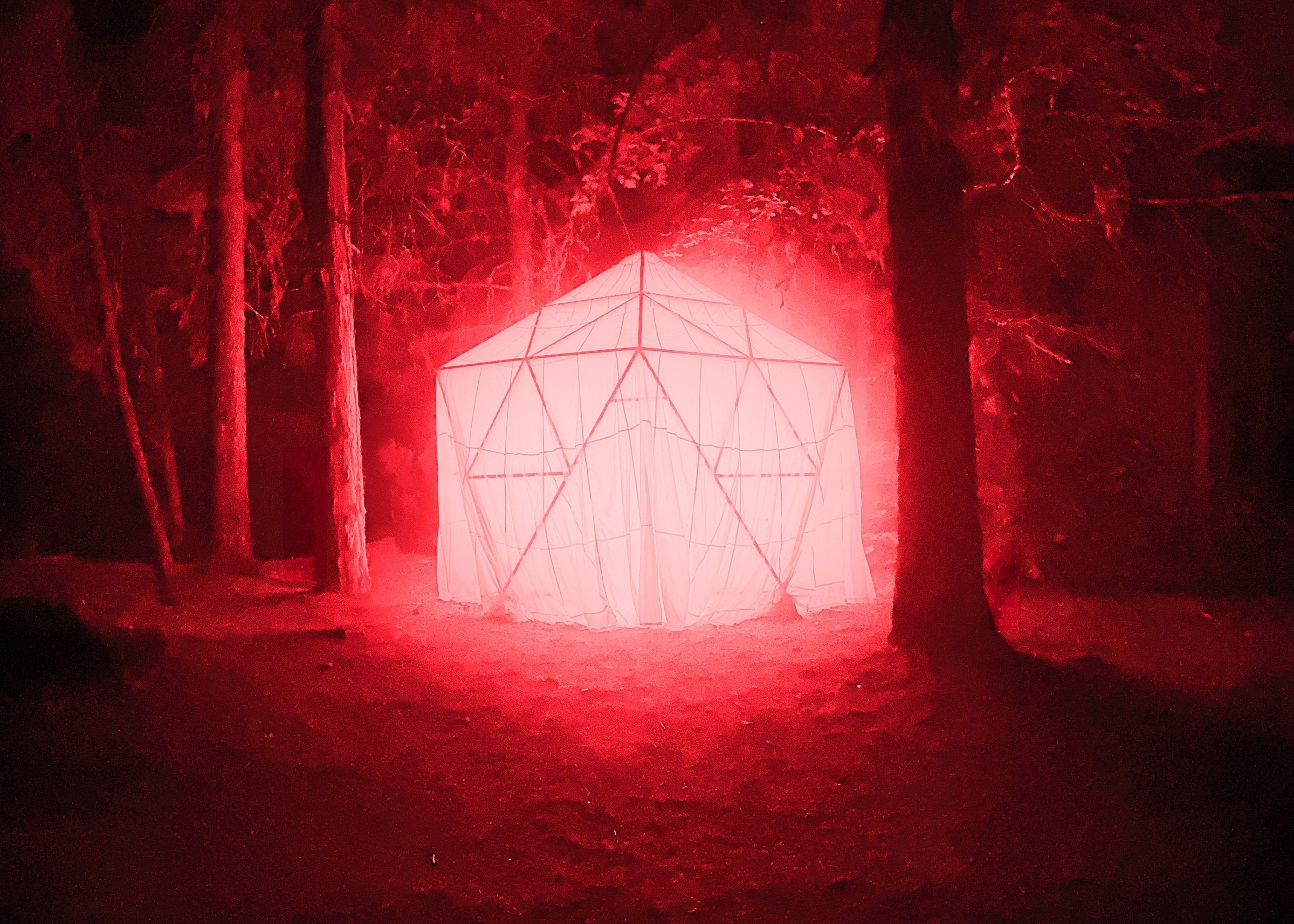 HoloDome3 glowing red in the forest, the parachute stretched over the wooden dome frame