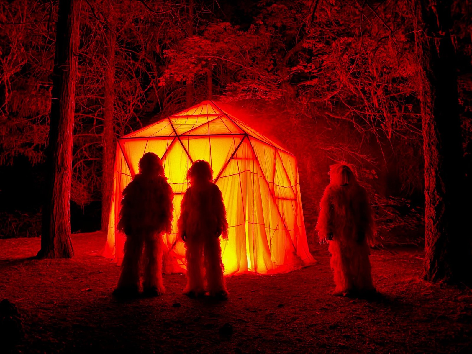 Three ghillie-suited figures standing before HoloDome3 glowing orange among the trees