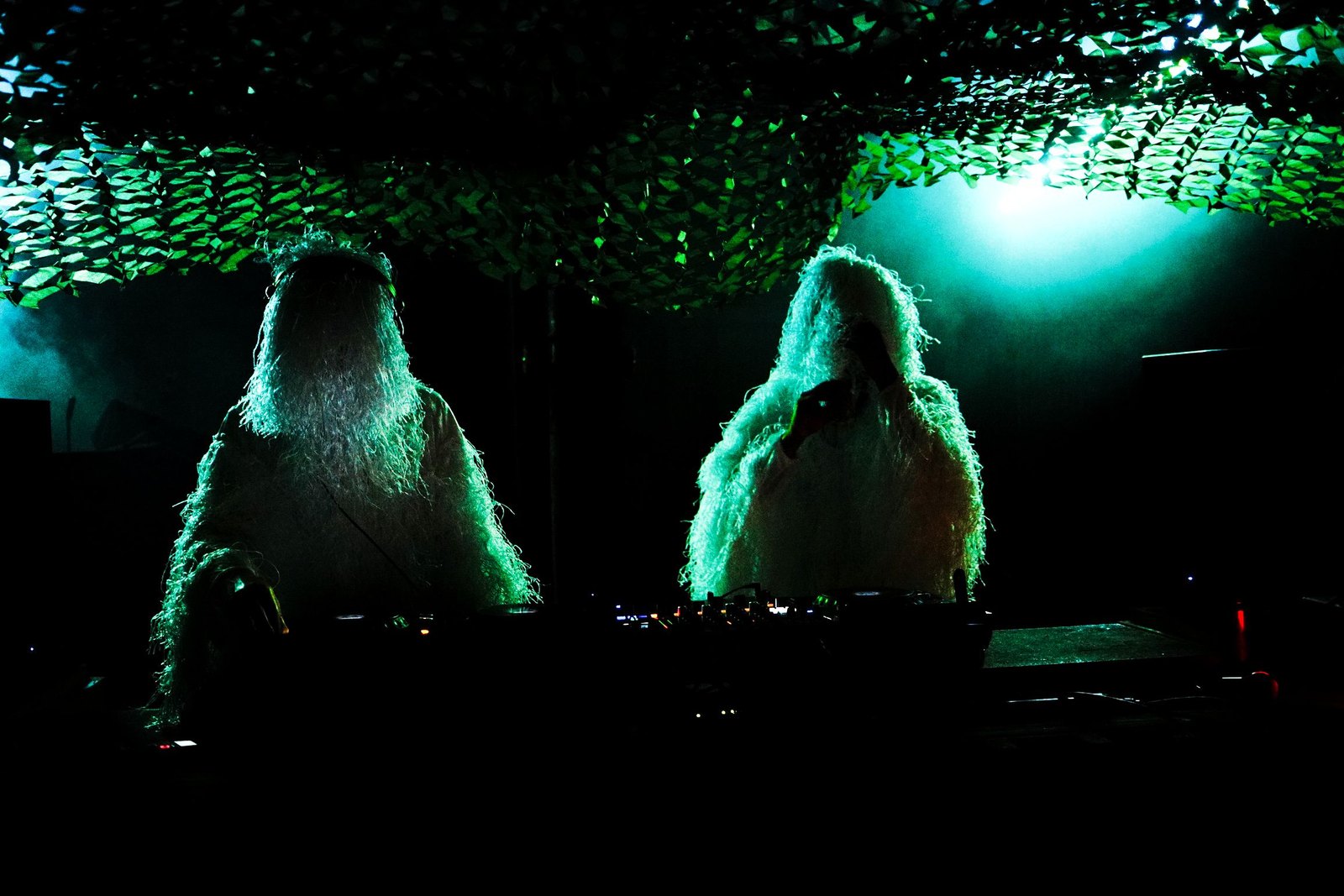 Two New Nostalgia members in white ghillie suits at the DJ decks, lit green