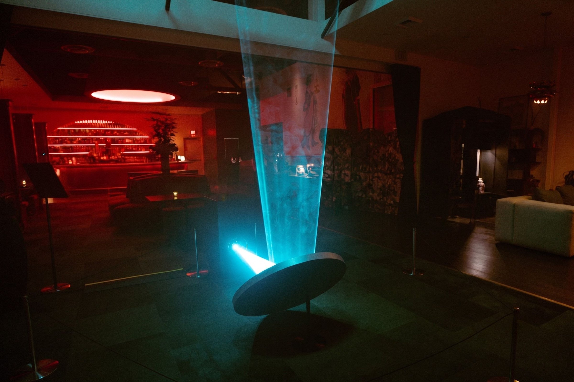 WaveGate’s beam in ice blue, rising from the mirror through haze in the lounge
