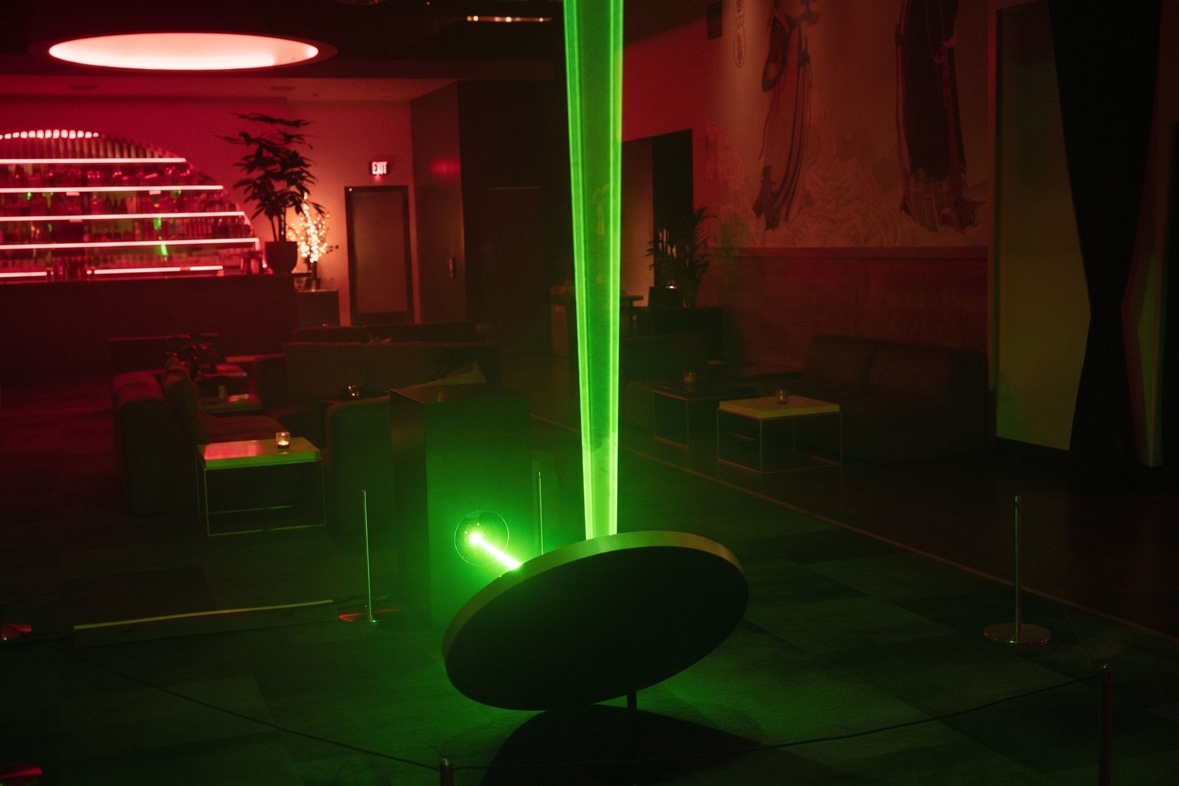 WaveGate at Moongate Lounge — a green laser beam rising from a round mirror on a black podium, red lights and the bar behind